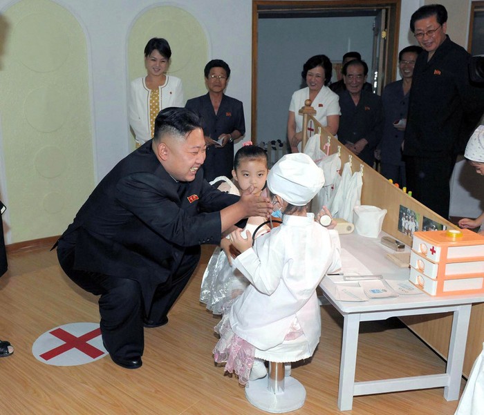 Tân Nguyên soái Kim Jong-un thăm phòng học cụ của trường mẫu giáo tươi cười rạng rỡ với các em bé, đằng sau là một phụ nữ áo trắng khá trẻ được giới truyền thông chú ý