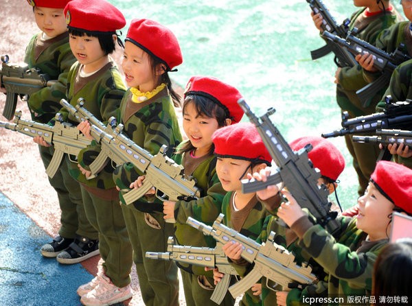 Những cô bé cậu bé tuổi mẫu giáo đã bị người lớn cho ôm súng AK to như thật