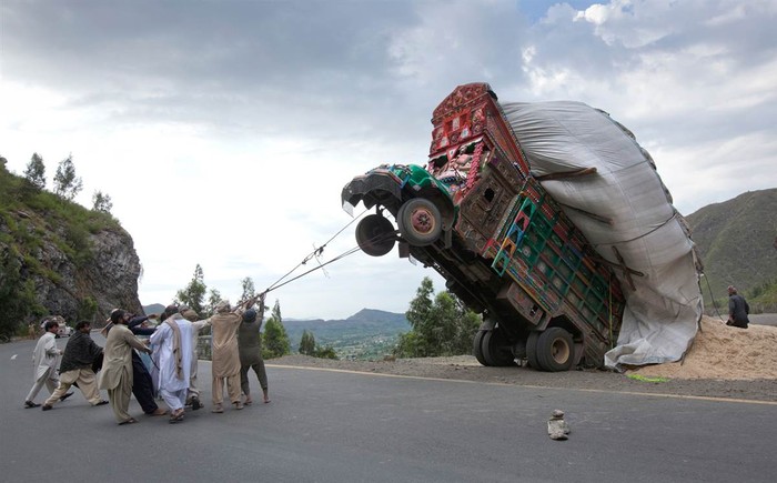 Những người đàn ông dùng dây thừng cố gắng để một chiếc xe tải bị dựng ngược vì đổ lúa mì, ảnh chụp ngày 13 tháng 4, dọc theo một con đường ở Dargai, ở quận Malakand, khoảng 100 dặm về phía tây bắc của đô Islamabad của Pakistan.
