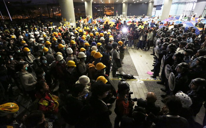 Người biểu tình mang mặt nạ, khẩu trang và mũ bảo hộ tập trung trước hàng rào cảnh sát ở trụ sở cơ quan lập pháp Hồng Kông đêm 18 rạng 19/11.