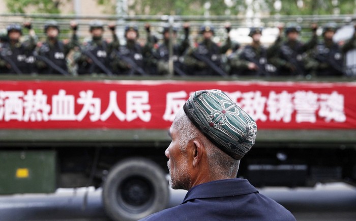 Một người đàn ông người Duy Ngô Nhĩ ở Tân Cương đang theo dõi hoạt động tuần tra chống khủng bố của chính quyền trên đường phố. Ảnh minh họa. Nguồn: SCMP.