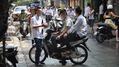 Trước cổng một trường THPT thuộc quận Đống Đa, Hà Nội một số nam sinh tóc cắt theo kiểu gọt hai bên tai, để bờm ở giữa hay dựng ngược tóc lên, tay phì phèo thuốc lá.