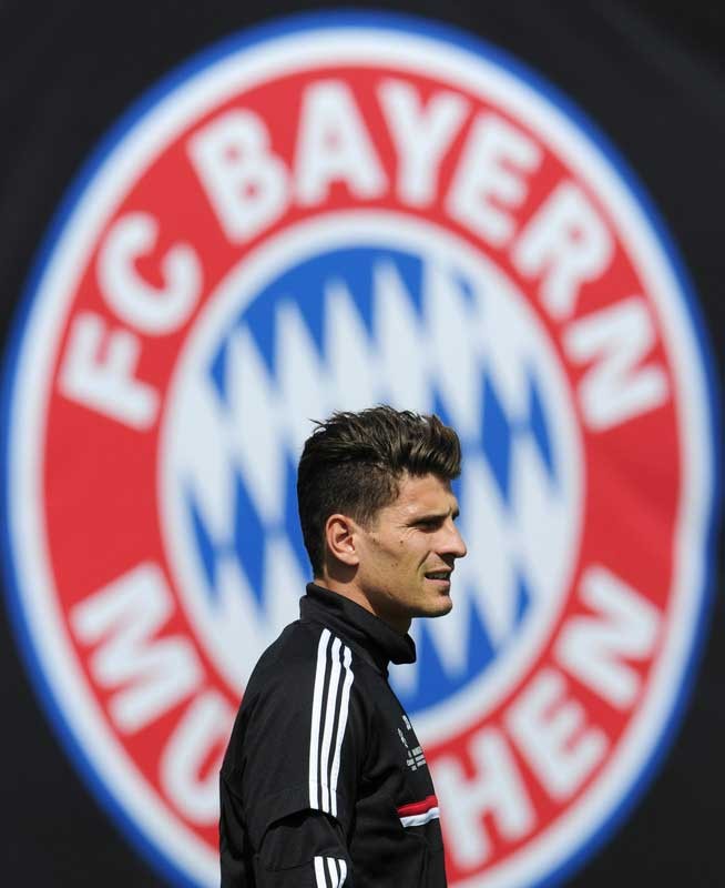 Mario Gomez bước ngang qua logo Bayern. Tiền đạo này có tỷ lệ 1.25 bàn thắng/trận khi thi đấu tại Allianz Arena.