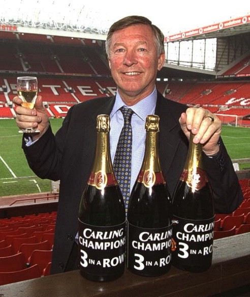 Sir Alex Ferguson bên cạnh 3 chai rượu tượng trưng cho 3 chức vô địch Premier League liên tiếp từ 1999 tới 2001 của Manchester United.