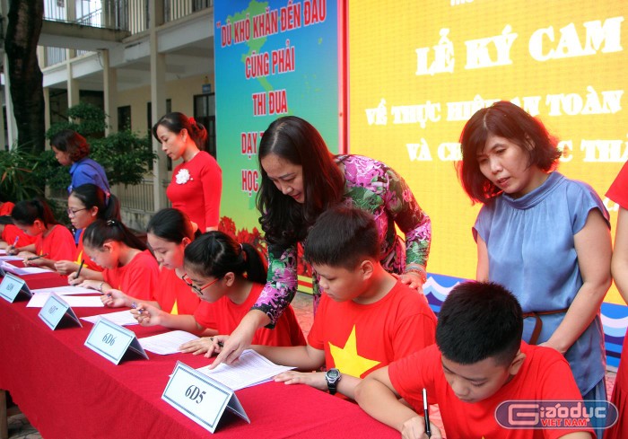 Cô giáo Nguyễn Thị Thu Hương, Hiệu trưởng nhà trường cùng các đại biểu chứng kiến các em học sinh ký cam kết chấp hành an toàn giao thông và giảm thiểu rác thải nhựa. (Ảnh: Lã Tiến)