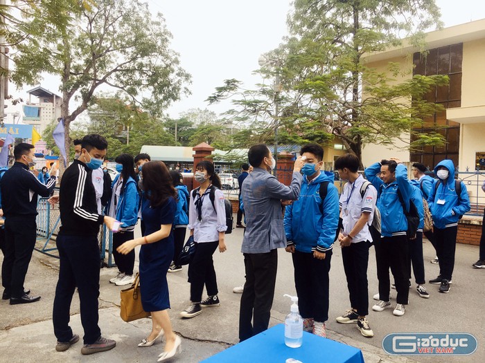 Giáo viên Trường Trung học phổ thông Hàng Hải kiểm tra thân nhiệt học sinh ngay tại cổng trường. (Ảnh: Lã Tiến)