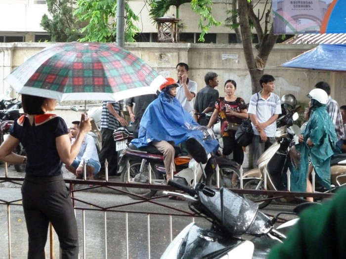Tại đường Hoàng Quốc Việt, trong lúc các thí sinh vào phòng thi, cơn mưa to bất chợt ập đến khiến các phụ huynh ướt sũng. (Xem đáp án môn Vật lí - Xem đáp án môn Toán)
