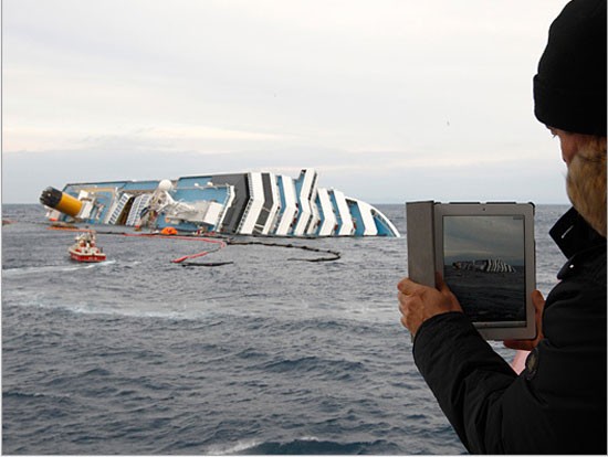 Một người đàn ông trên phà đang dùng iPad để ghi lại những khoảnh khắc cuối cùng của chiếc tàu Costa Concordia trước khi nó bị chìm sâu xuống lòng biển vùng Giglio, Italia.