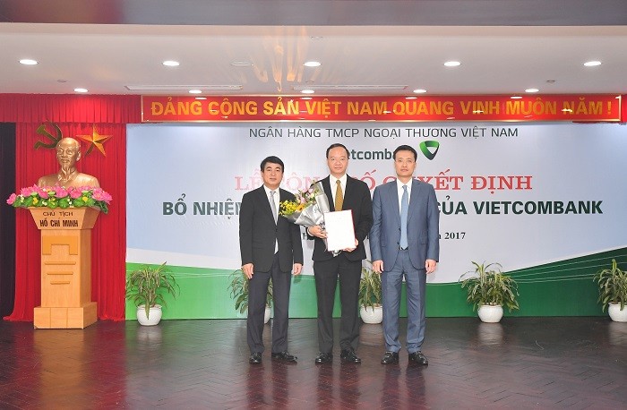 Chủ tịch Hội đồng quản trị Vietcombank Nghiêm Xuân Thành (bên trái) và Tổng Giám đốc Vietcombank Phạm Quang Dũng (bên phải) trao Quyết định và tặng hoa chúc mừng Ông Lê Quang Vinh – tân Phó Tổng Giám đốc Vietcombank.