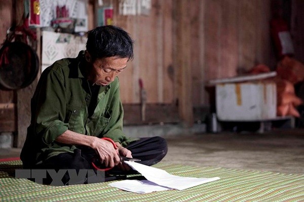Nghi thức cắt giấy để dán lên các công cụ lao động của người Mông. (Ảnh: Hữu Quyết/TTXVN)