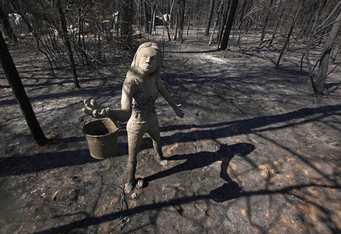 Một bức tượng đang cầm chiếc xô nước đứng trước một ngôi nhà bị cháy rừng quyét qua và thiêu rụi ở hạt Bastrop, Texas ngày 6/9/2011.