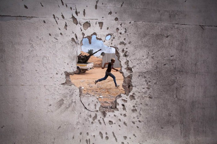 Ảnh chụp một binh sỹ nổi dậy chạy vụt qua lỗ thủng bị đạn bắn ở Sirte, Libya.