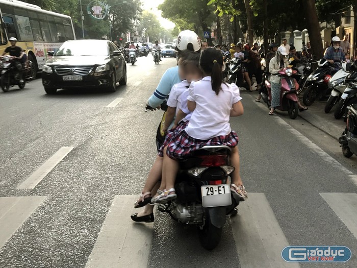 Trước cổng Trường tiểu học Phan Chu Trinh, phụ huynh đi ngược chiều và không đội mũ bảo hiểm cho 3 trẻ. Ảnh: Tùng Dương.