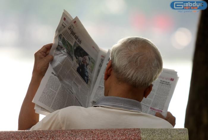 Một ông cụ ngồi đọc báo mới ra.