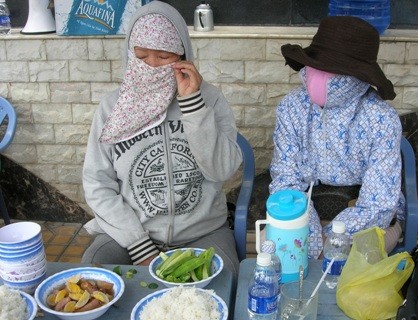 Bà N (trái) luôn bịt kín khẩu trang. Nữ doanh nhân này chỉ mở ra khi ăn cơm, uống nước trước lều bạt căng ngay cổng biệt thự đại gia thủy sản Diệu Hiền. Ảnh: Trúc Linh