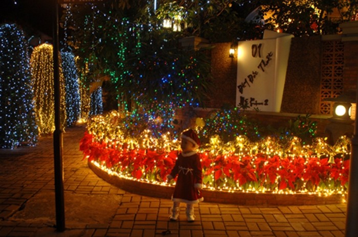 Một em bé mặc đồ Giáng sinh đang đứng trước vườn hoa chờ bố mẹ chụp ảnh.