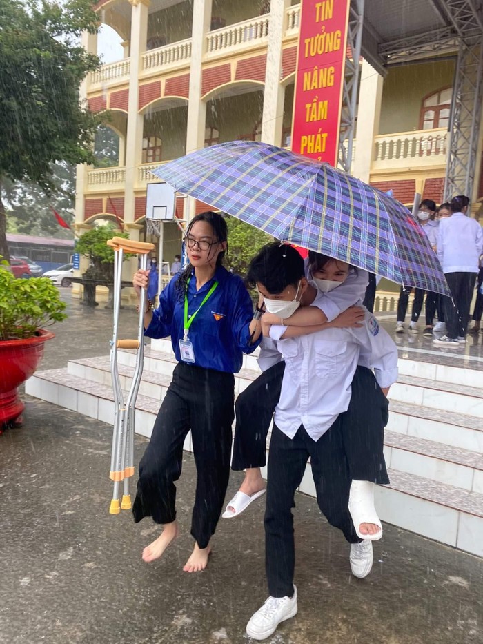 Không ngại mưa lớn, sinh viên tình nguyện hỗ trợ một thí sinh bị gãy chân đến và rời điểm thi an toàn (Ảnh: CTV)