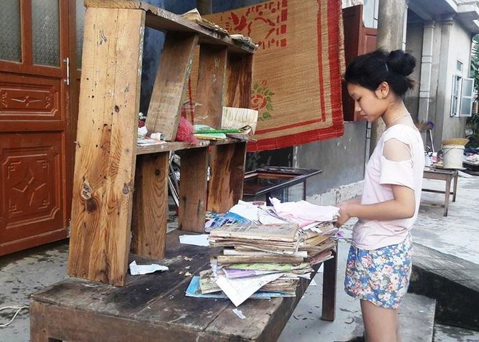 Em Nguyễn Thị Vân Nga mang sách vở ra sân phơi, cố lật dở, kiểm tra lại đống sách vở bị ướt nhẹp (Ảnh: T.P)