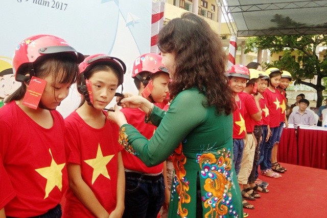 Thứ trưởng Nguyễn Thị Nghĩa đội mũ bảo hiểm cho các em học sinh tỉnh Quảng Bình. (Ảnh: P. T)