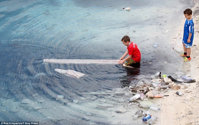 Một cậu bé nghịch nước bên cạnh đống rác thải ven bờ