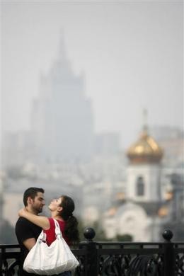 Một đôi nam nữ đang ôm nhau với hình ảnh phía sau là các tòa nhà bị bao phủ trong sương mù.