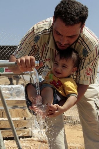 Một người cha đang rửa chân cho đứa con nhỏ của mình ở trại tị nạn.