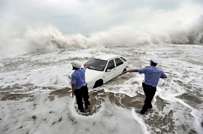Cảnh sát hướng dẫn một chiếc xe hơi bị mắc kẹt trên con đường ngập nước khi cơn bão Boloven tấn công Thanh Đảo, tỉnh Sơn Đông, Trung Quốc.