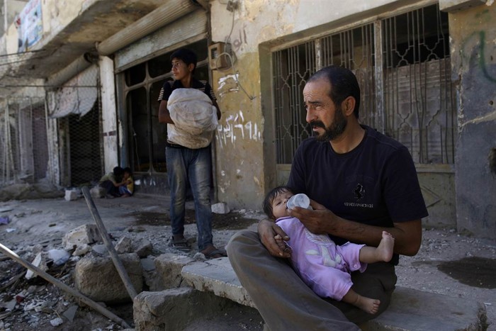Một người đàn ông Syria cho con gái của mình uống sữa khi đang ngồi ở phía trước ngôi nhà của mình đã bị tàn phá ở Azaz, vùng ngoại ô Aleppo, Syria.