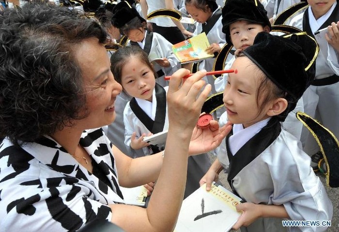 Một giáo viên của trường tiểu học đền Khổng Tử Nam Kinh dùng bút son chấm lên trên trán của học sinh, biểu tượng cho sự thông thái, trong buổi lễ bắt đầu năm học mới được tổ chức tại đền thờ Khổng Tử ở Nam Kinh, tỉnh Giang Tô.