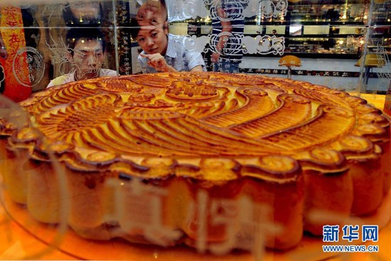 Hai khách hàng đang chiêm ngưỡng chiếc bánh khổng lồ được trưng bày tại một cửa hàng ở Thẩm Dương, tỉnh Liêu Ninh, đông bắc Trung Quốc. Chiếc bánh trung thu khổng lồ có đường kính 1 mét được nướng với một hình rồng và chim phượng hoàng trên bề mặt. Các đầu bếp phải bỏ ra nửa tháng để hoàn thành chiếc bánh khổng lồ này, trong đó có 31,5 kg nhân và 13,5 kg bột.
