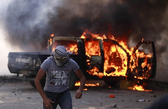 Một người biểu tình ở Cairo, Ai Cập chạy xa ra khỏi một chiếc xe cảnh sát đang cháy trong cuộc đụng độ với cảnh sát chống bạo động, gần Đại sứ quán Mỹ.