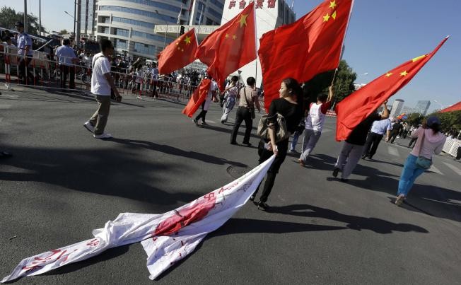 Một người phụ nữ Trung Quốc kéo lá cờ Nhật Bản trên mặt đất trong một cuộc tuần hành phản đối gần Đại sứ quán Nhật Bản tại Bắc Kinh.