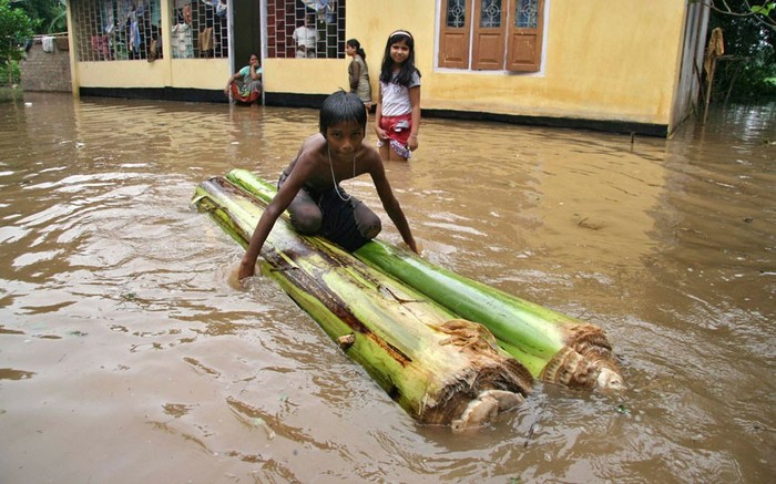 Một cậu bé ngồi trên một chiếc bè chuối bên ngoài ngôi nhà bị ngập nước ở vùng ngoại ô thành phố Guwahati.