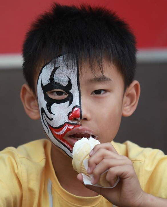 Một bé trai được vẽ mặt nạ và đang ăn kem trong khu vui chơi Happy Valley ở Bắc Kinh.