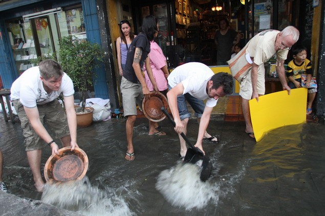 Khách du lịch nước ngoài giúp người dân Bangkok tát nước ra khỏi cửa hàng trên đường Samsen.