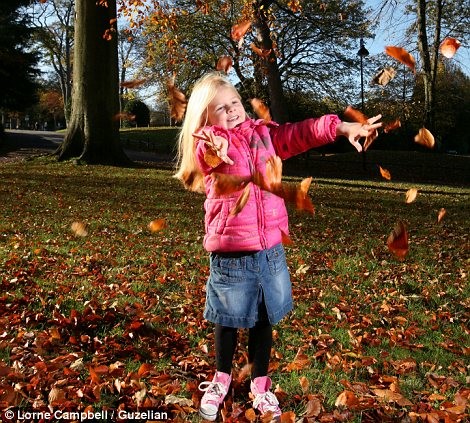 Bé Ella , 5 tuổi, nghịch lá vàng trong công viên Lister trong sớm mùa thu