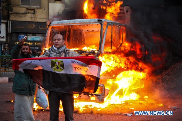 Người biểu tình giương cờ trước một chiếc xe cảnh sát bị đốt cháy ở Cairo hôm 19/11/2011