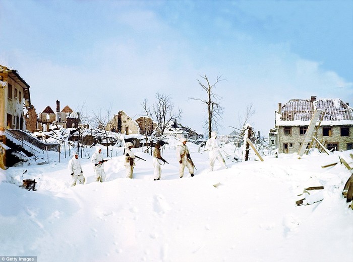 Những người lính Anh thuộc Sư đoàn 7 mệt nhọc đi lại trong tuyết băng qua một ngôi làng của Bỉ bị ném bom vào năm 1945