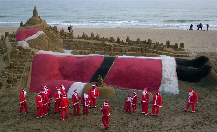 Các ông gia Noel ngắm nhìn một ông già Noel khổng lồ làm bằng cát trên bãi biển Puri, Ấn Độ
