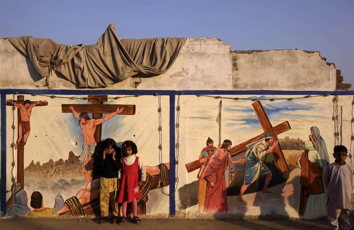 Hai bé gái Pakistan đứng cạnh bức tranh vẽ trên tường cảnh Chúa Giê-su bị đóng đinh trên cây thập giá ở Islamabad, Pakistan