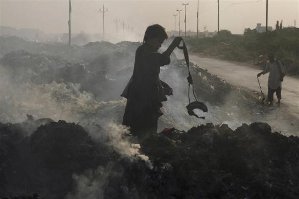 Cậu bé người Pakistan đang giữ cục nam châm trong khi một người khác cố tìm kiếm các vật liệu có thể tái chế được tại bãi rác ở Karachi ngày 26/10/2011