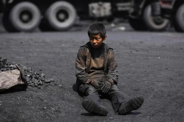 Một cậu bé mình mẩy lấm lem than bụi ngồi bệt xuống mặt đất đen sì tại bãi khai thác than ở Changzhi, tỉnh Sơn Tây, Trung Quốc ngày 1/7/2008