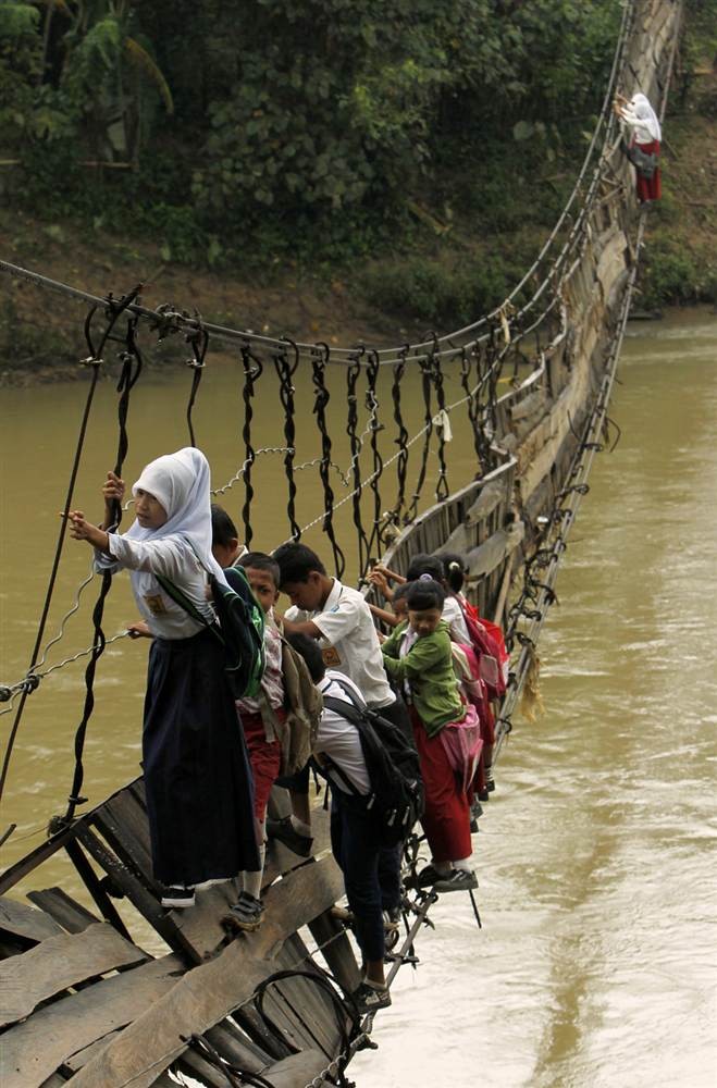 Học sinh tại làng Sanghiang Tanjung, Banten, Indonesia bám vào dây cáp cầu treo đã sụp đổ để băng sông tới trường hôm 19/1.