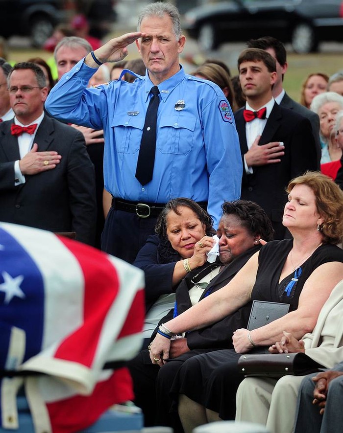 Wade Johnson đứng bên cạnh người vợ, người đang cố lau giọt nước mắt cho em dâu trong tang lễ của người em trai Roger, người bị một nhân viên cảnh sát bắn chết khi kiểm tra một chiếc xe đáng ngờ tại Mỹ, hôm 28/1.