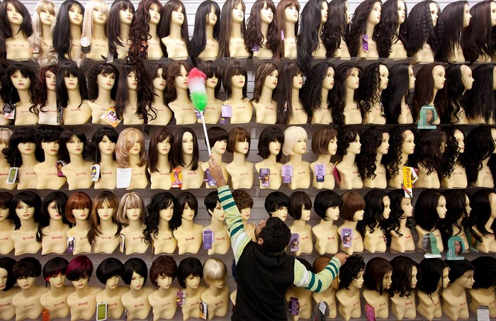 Một người đàn ông đang phủi bụi trên những ma-nơ-canh mang tóc giả của một hiệu làm tóc và thẩm mỹ tại Brixton, London, Anh ngày 2/2.