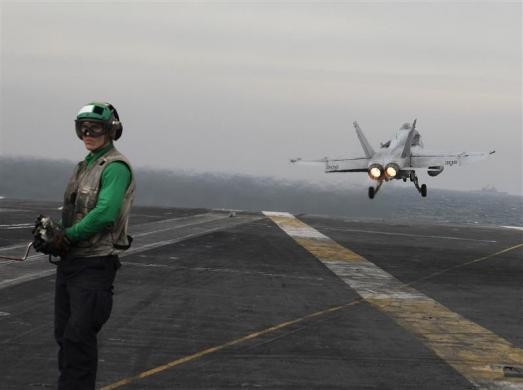 Một phi công đứng trước chiếc máy bay F/A-18C Hornet đang cất cánh từ tàu USS Abraham Lincol hôm 13/2/2012