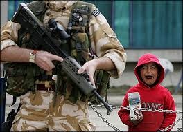 Một em bé Afghanistan khóc sau hàng rào, nơi binh sĩ NATO đang đứng gác với súng.