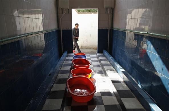 Một người dân chuẩn bị bước vào nhà vệ sinh của một trường tiểu học địa phương, nơi đặt các chậu thu thập nước tiểu của các bé trai tại Dongyang ngày 26/3/2012