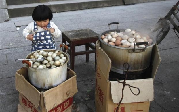 Một bé gái đang nhìn chằm chằm vào nồi trứng luộc bằng nước bình thường bên cạnh nồi trứng luộc bằng nước tiểu của các bé trai tại Dongyang ngày 26/3/2012
