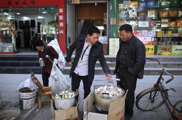 Ge Yaohua 51 tuổi (phải) - một người bán trứng đang nhìn vị khách chỉ tay chọn mua trứng trong nồi trứng luộc bằng nước tiểu bé trai tại Dongyang ngày 26/3/2012